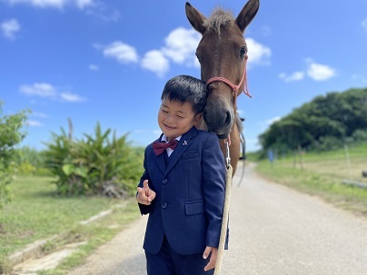 顔を寄せる馬に笑顔を浮かべる男児の写真